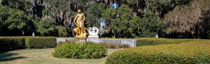 Gold statue of a man and jungle cat surrounded by lush gardens.