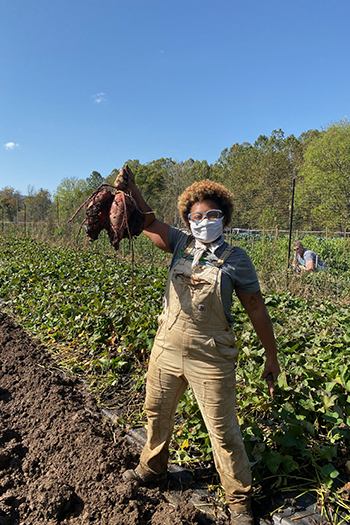 new garden manager sadia pollard holds up vegetables harvest from a garden
