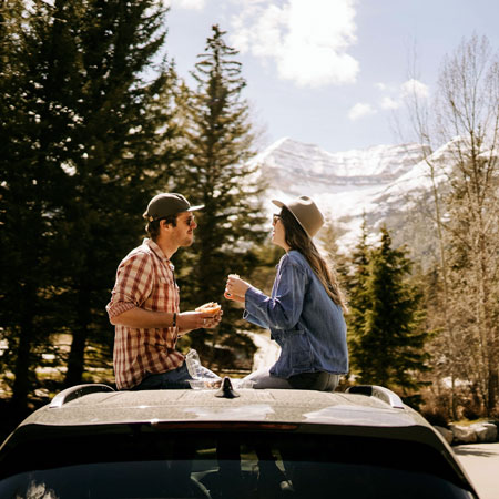 man and woman sit on top of car eating in mountain setting