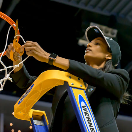 cynthia jordan stands on a ladder to cut a piece of the basketball net after a major win