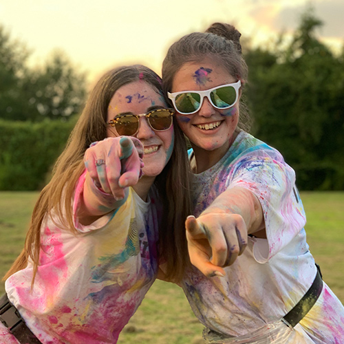 Cecelia Tatro and her friend pointing at the camera covered in chalk from a color run.