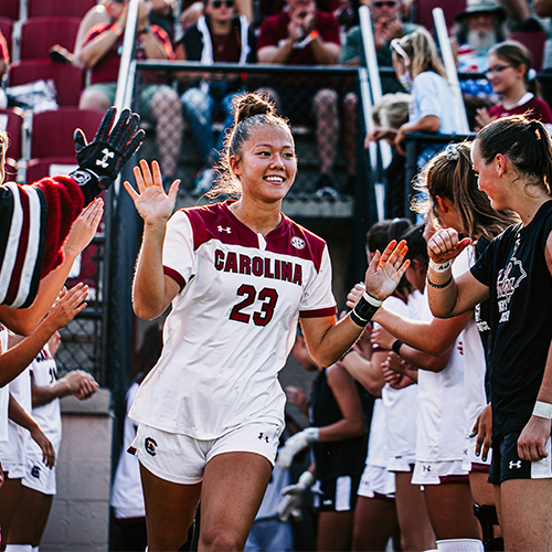 Samantha Chang high-fives with teammates walking out of the locker room onto the soccer field. 