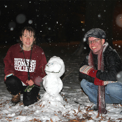 Riley Sutherland and her friend sit beside the snowperson they made on the horseshoe.
