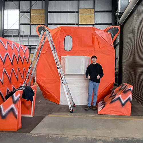 a man stands in front of pieces of a wood and paper tiger