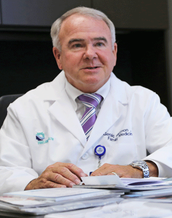 Dr. Gerald Harmon in white medical coat and purple-striped tie.