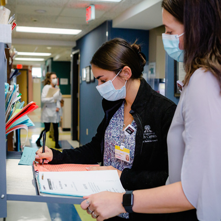 two women wearing masks work in a medical setting