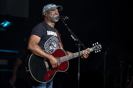 Darius Rucker stands on stage playing a guitar and singing into a microphone