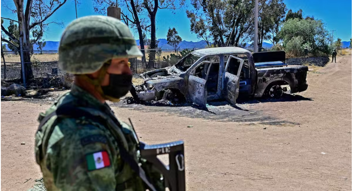 A soldier standing in front of a burned pickup truck