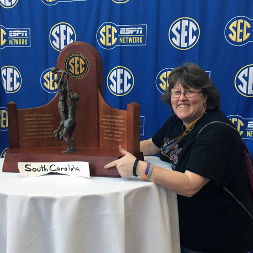 woman stands next to the SEC women's basketball trophy pointing to a handmade south carolina sign in front with a backdrop that has the espn sec network logo