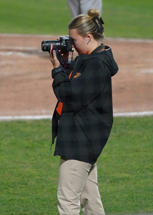 Hannah Proce on a baseball field taking pictures with a camera.