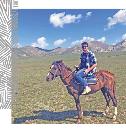 Josh hughes sits on a horse in front of mountains.