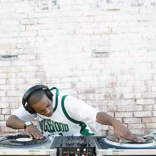 a man "scratches" on two turntables in front of a white brick wall