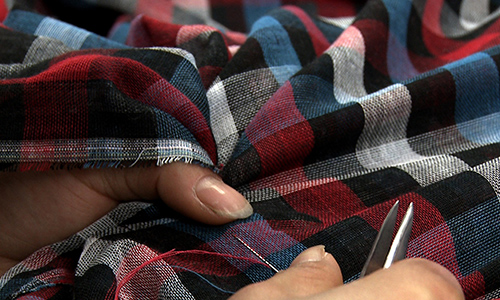 Close up of a person's hands working on a fabric using a needle and thread.