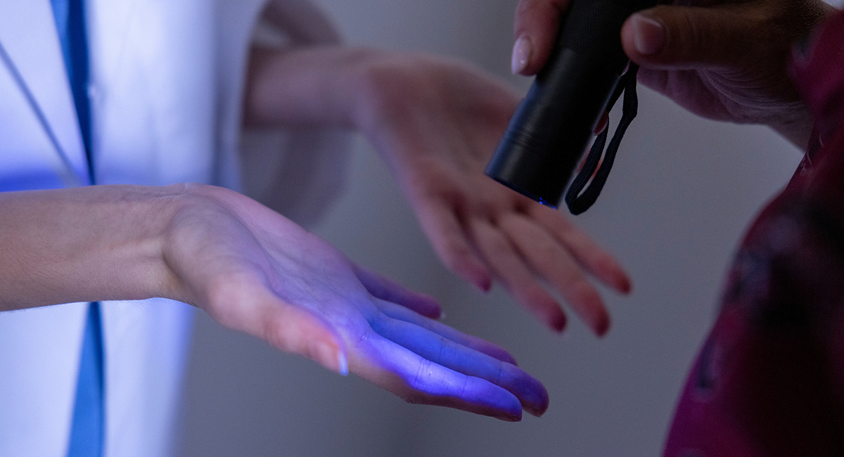 An ultraviolet flashlight is used to examine hands for germs.