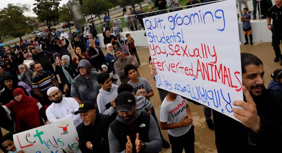 A group of protesters standing outside a library; one carries a sign that says 'Quit grooming students, you sexually perverted animals'" 