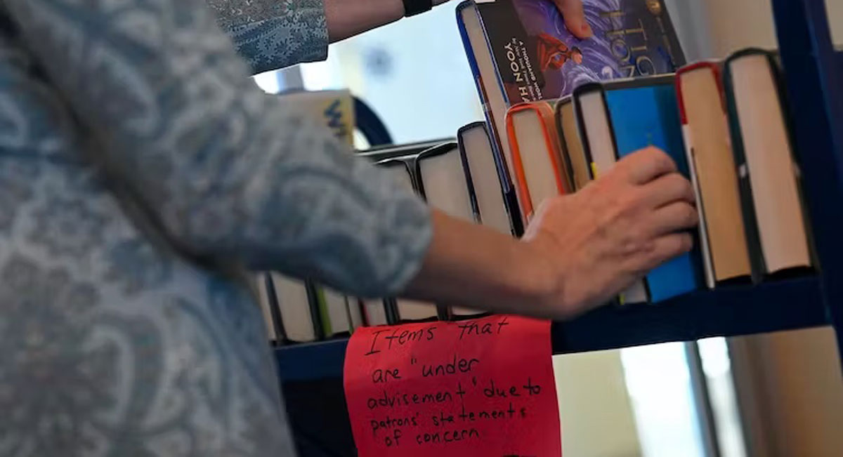 A woman stands next to a book cart and touches some of the books.