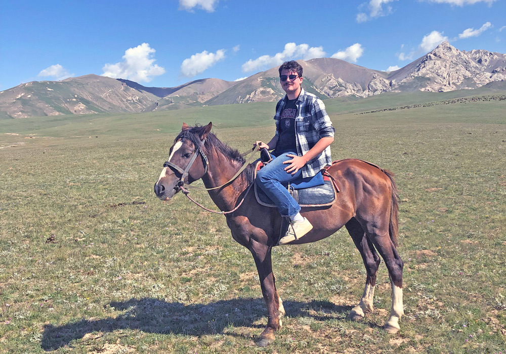 Josh Hughes sits on a horse, mountains in back