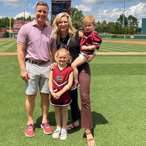 James and Natalie Wolf stand on the USC baseball field with their two children.