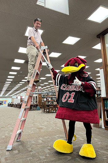 USC mascot cocky hands light bulb to man on ladder