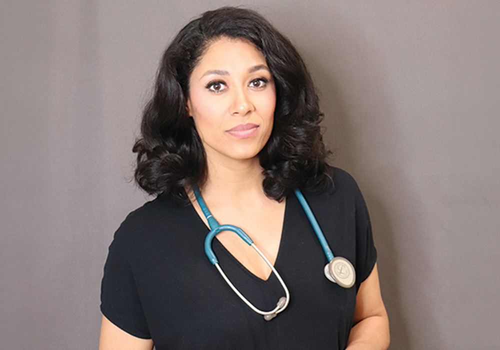 woman stands in hospital scrubs with a stethoscope around her neck