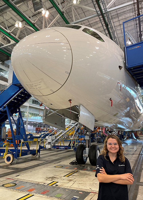 USC aerospace engineering major Ashley Poyner stands in front of an under-construction 787 in an airplane hanger.
