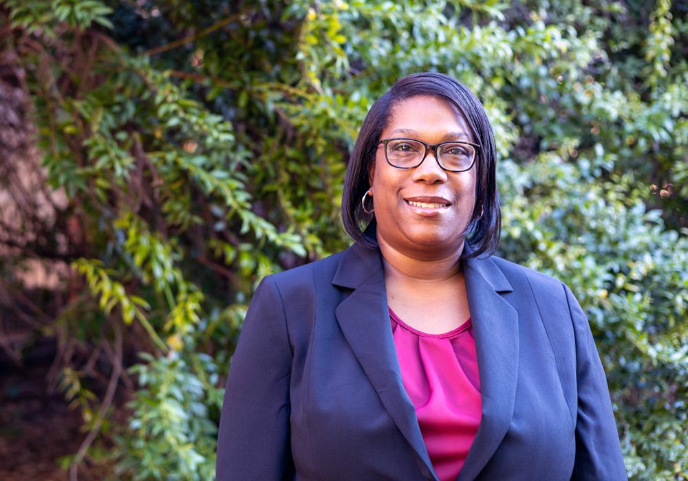 woman stands outside with a tree and building in the background