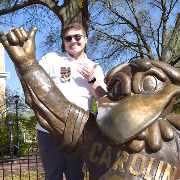 Greyson Carraway stands with the Cocky statue on campus