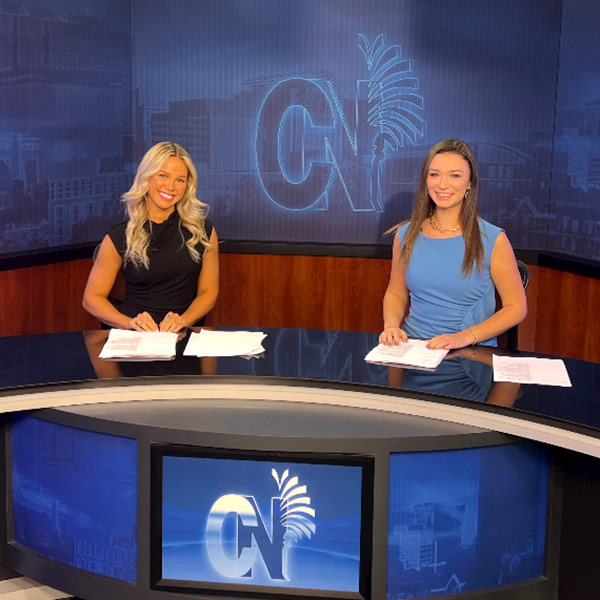 Haley Bowick sits at the Carolina News anchor desk with another student.