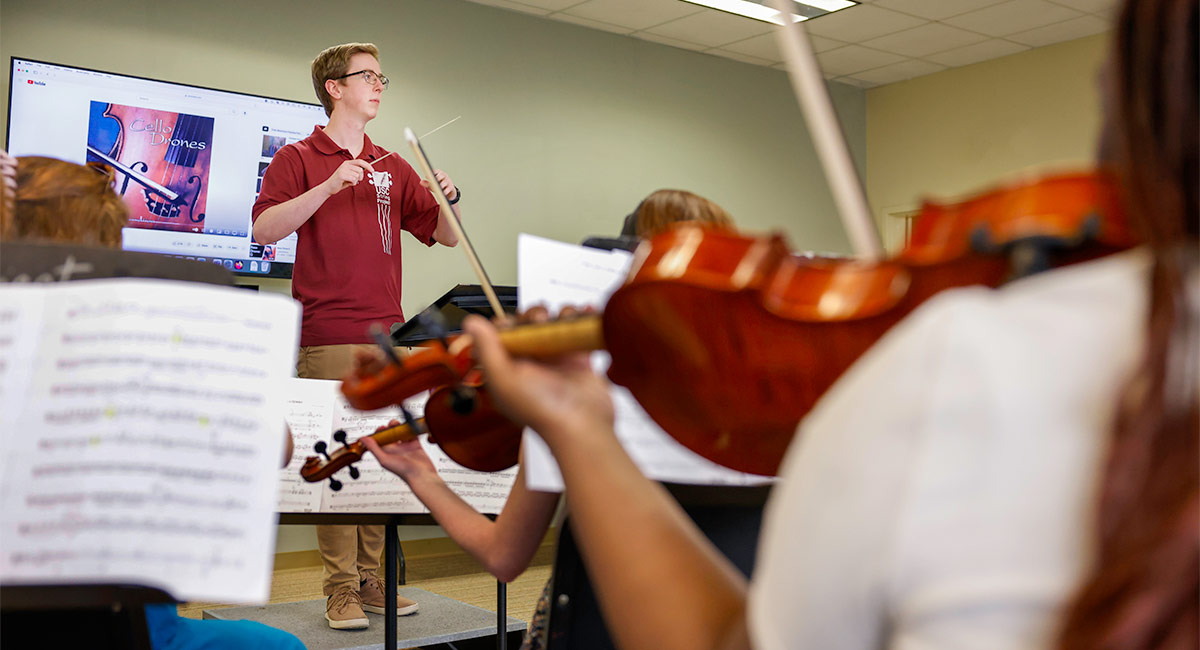 Teacher conducts students playing string instruments