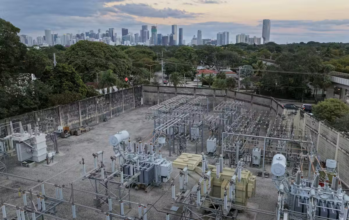 An aerial view of metal equipment and wires with a city skyline in the background.&nbsp;