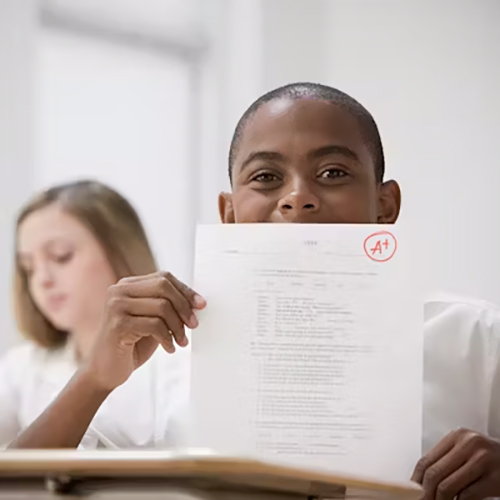 A young boy proudly displays his test marked with a score of A+.