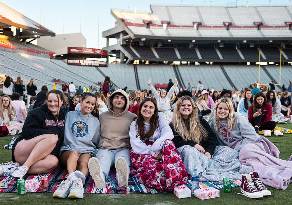 six students sitting on field at stadium watching movie