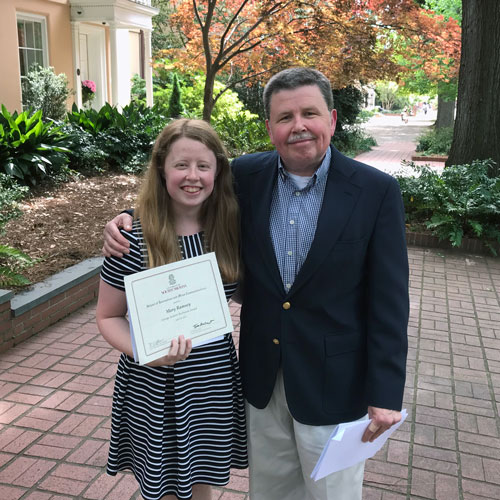 two people stand outside with a building and trees in the background