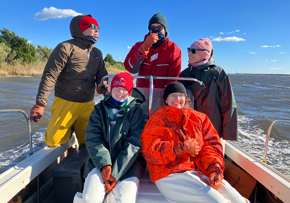Five researchers bundled up in coats and hats against the cold air aboard a boat on Winyah Bay