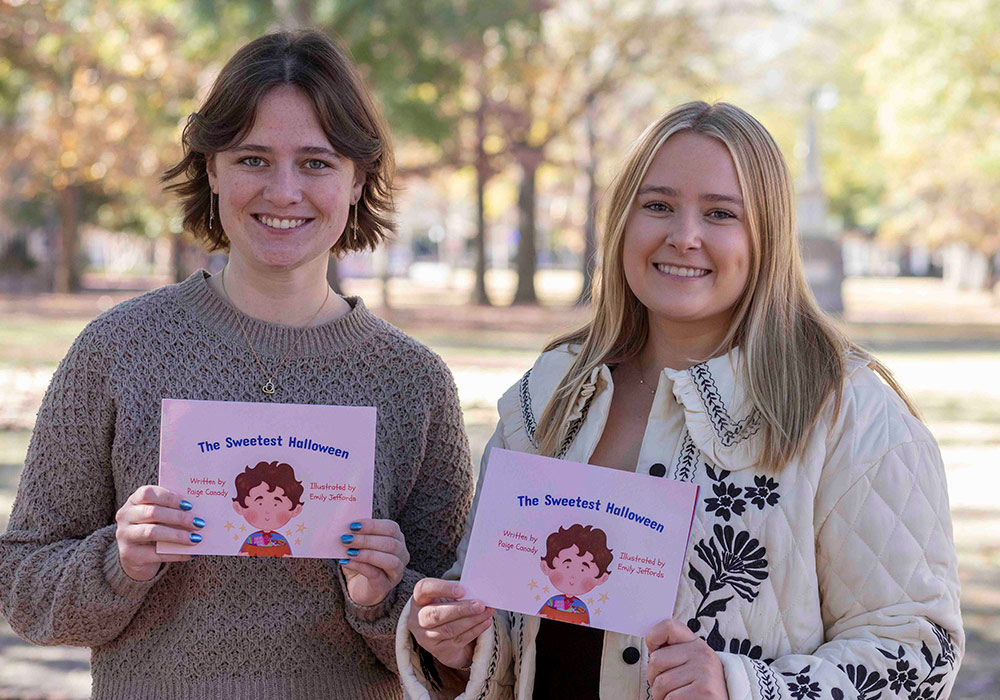 Two students standing outdoors holding a children's book