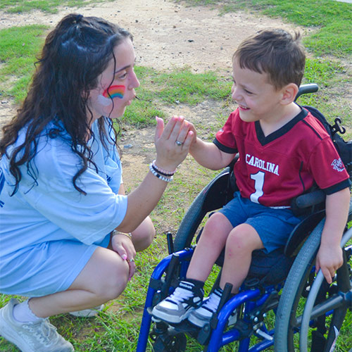 girl kneels down to interact with a child in a wheelchair