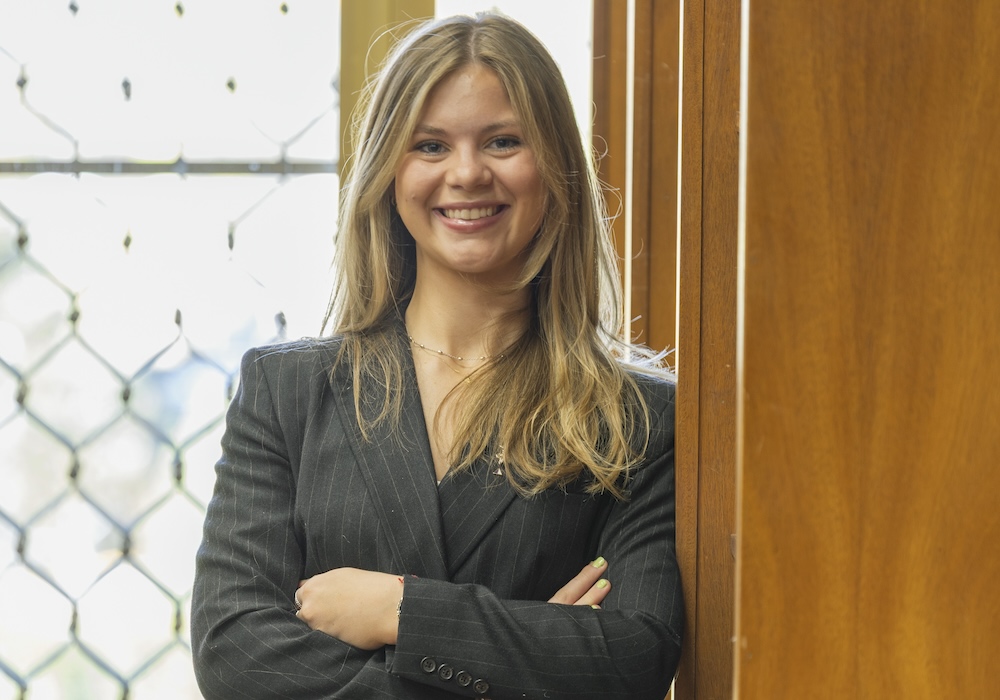 ansley martin in gray suit with arms crossed leaning against a wall