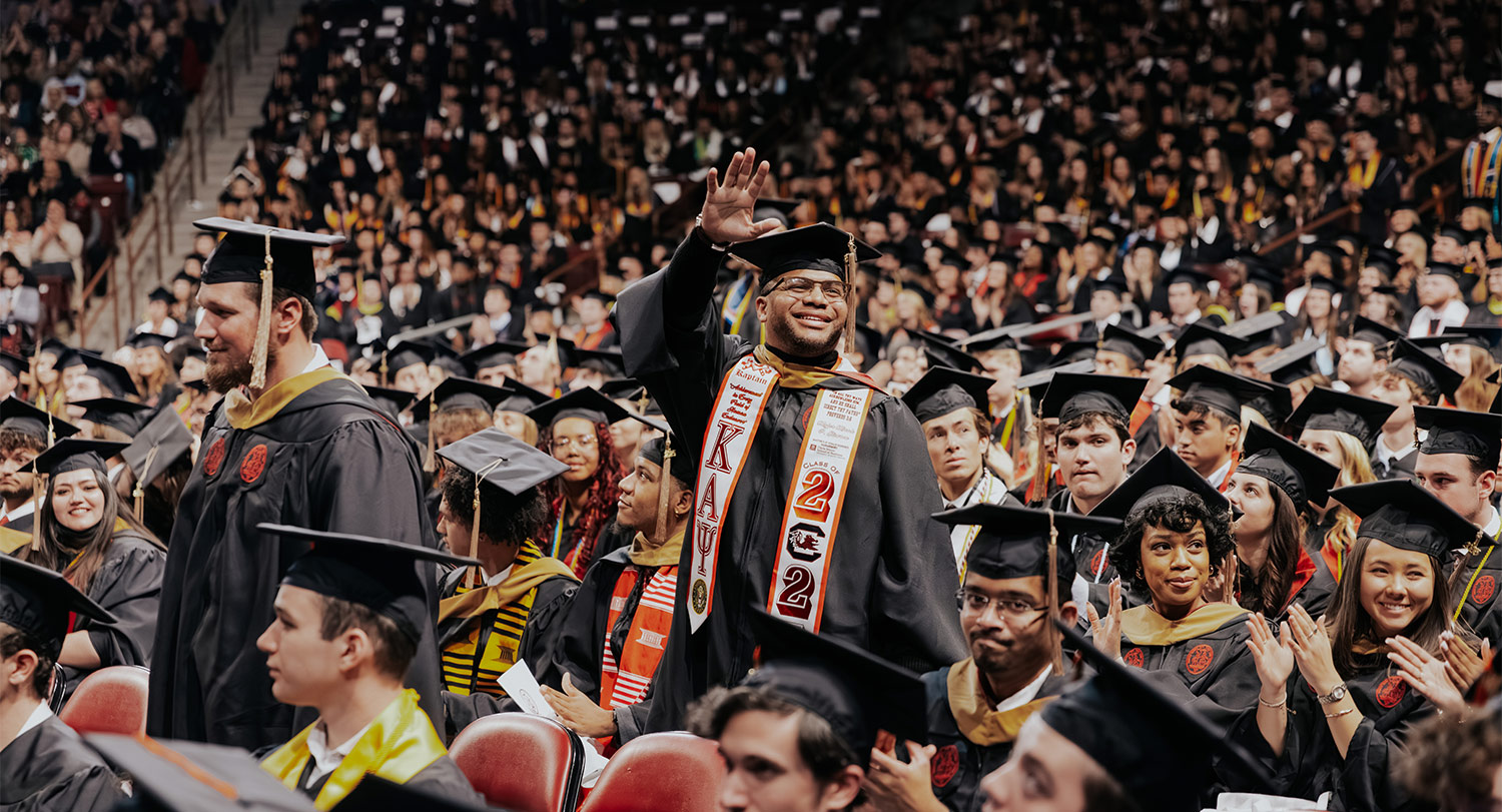 Graduate waves in midle of commencement crowd