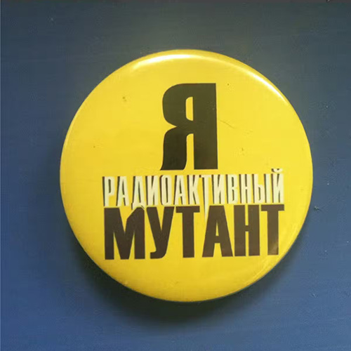 A round yellow pin with Russian characters in black and white stating "I am a radioactive mutant."