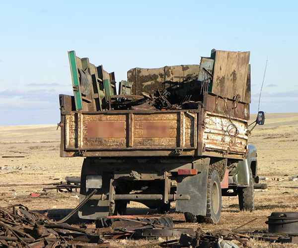 An older, rusty truck drives across an arid tundra filled with salvaged metal scraps from the former nuclear test site.