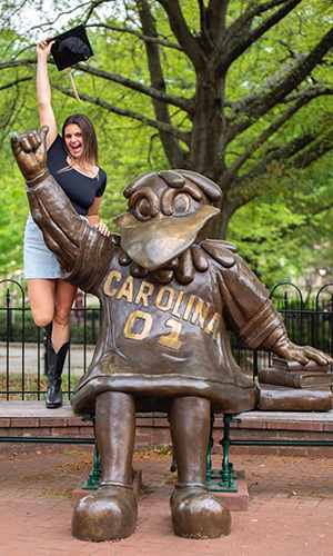 Olivia Gott stands next to the Cocky statue while holding a graduation cap.