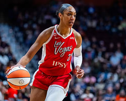 A brown-skinned basketball player in red Las Vegas jersey dribbles orange and white basketball