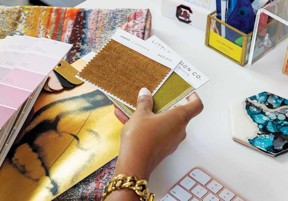 Amber Guyton (hands view) looks through swatches of fabric in her home office.