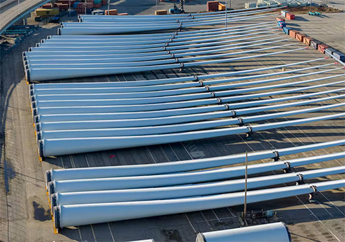 An aerial view of uninstalled wind turbine blades laid horizontally on flat land