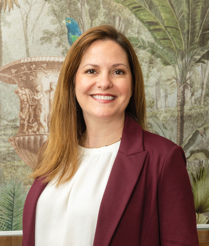 Emily Farr poses for a portrait in front of a mural wearing a white shirt and red blazer.
