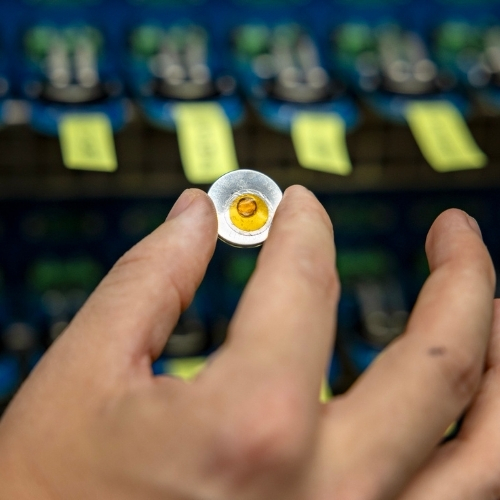 A hand holds a small battery in a science lab.
