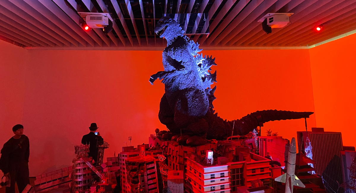 A model of Godzilla towers over a city scene in an exhibition room lit with red light.