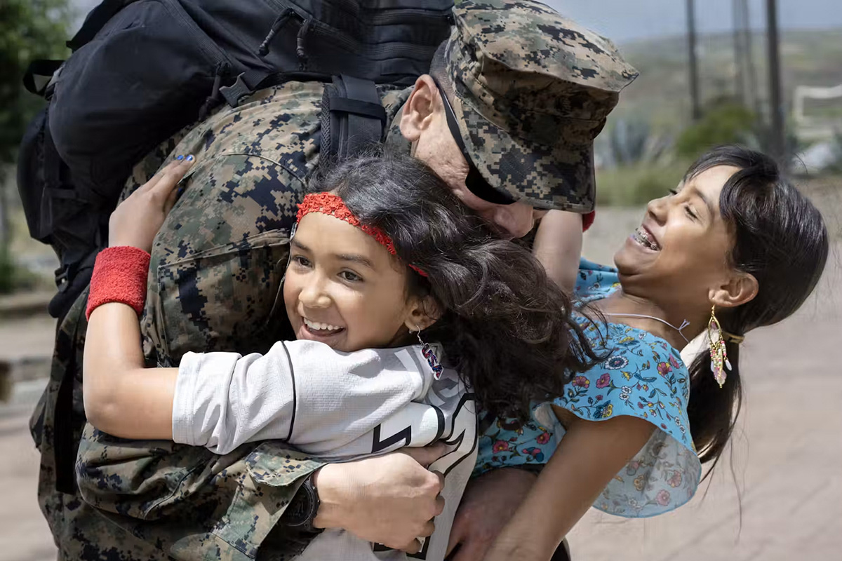 A man wearing a military uniform hugs two girls who are smiling.