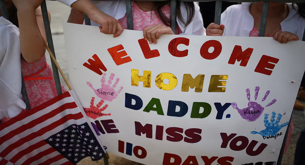 A sign next to an American flag says, 'Welcome home daddy, we miss you 110 days.'