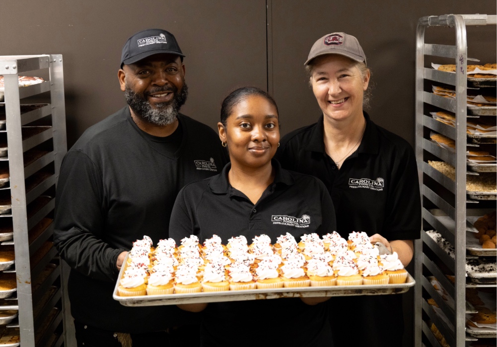 Bakers of the USC bakeshop pose for a picture with a tray of cupcakes.